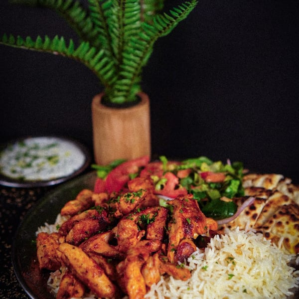 Mediterranean chicken and rice platter with salad, naan bread, and a side of yogurt sauce.