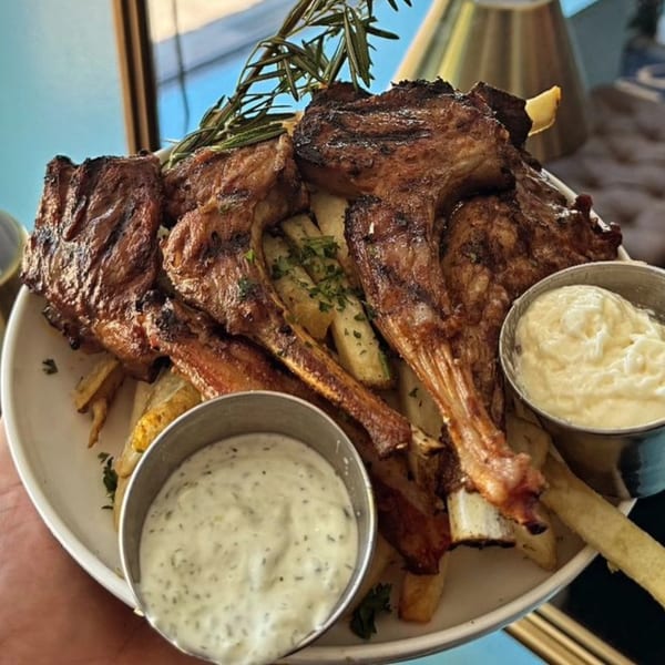 Grilled Mediterranean lamb chops with fries, rosemary, and two dipping sauces on a white plate.