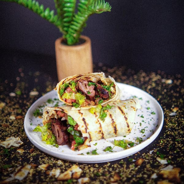 Two grilled Mediterranean wraps filled with meat, lettuce, and tomatoes on a white plate.