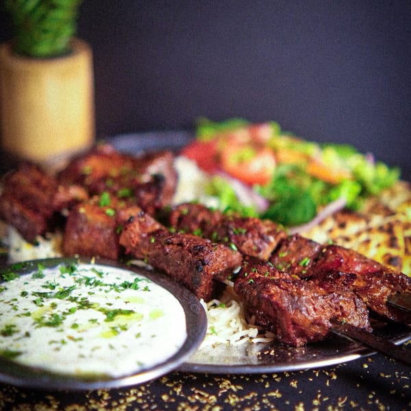 Grilled Mediterranean meat skewers with rice, salad, and a side of white sauce with herbs.