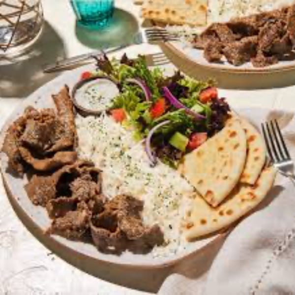 A Mediterranean gyro platter with meat, rice, salad, pita bread, and tzatziki sauce.