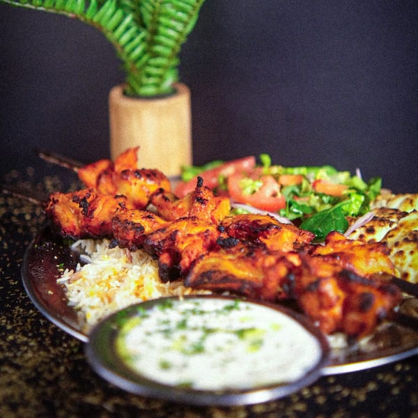 Grilled chicken skewers with rice, salad, and a side of white sauce on a metal platter.